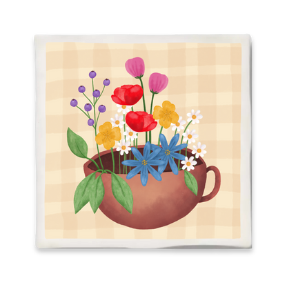 Decoratief keramisch tegeltje met een illustratie van een mok gevuld met kleurrijke bloemen op een beige geruite achtergrond. Formaat 10x10 cm, voorzien van haakje om op te hangen."